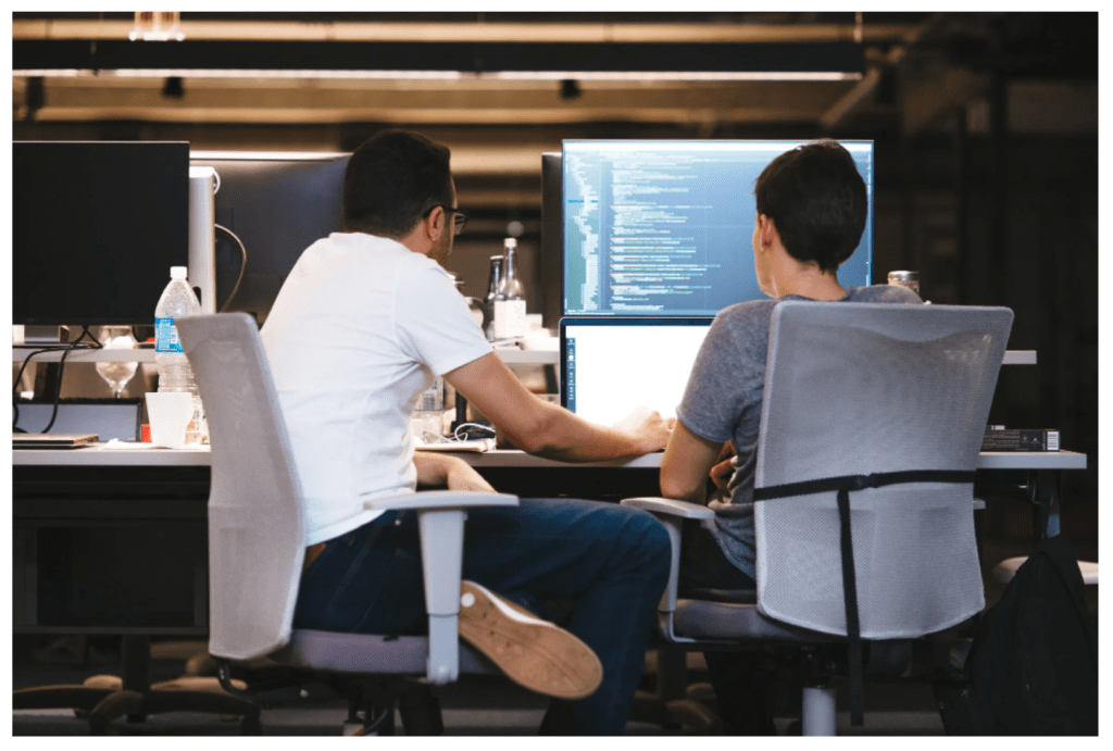 Equipo de ingeniería de Nu. Dos hombres trabajan frente a una computadora en segundo plano.