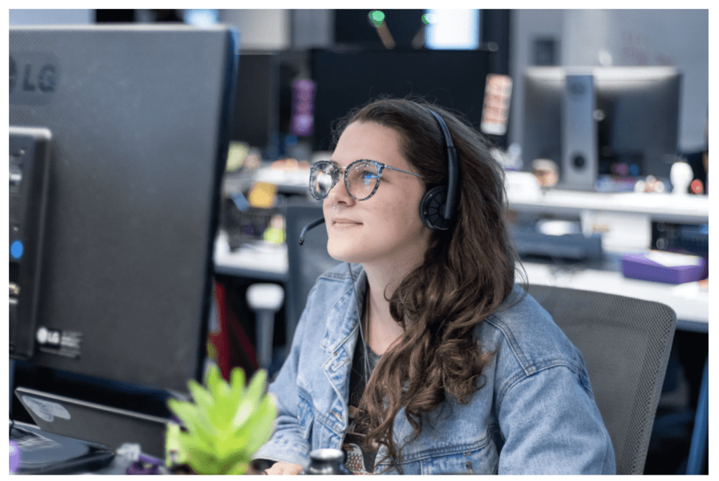 Una chica con anteojos grandes y campera de jean mira atentamente a la pantalla de su computadora.