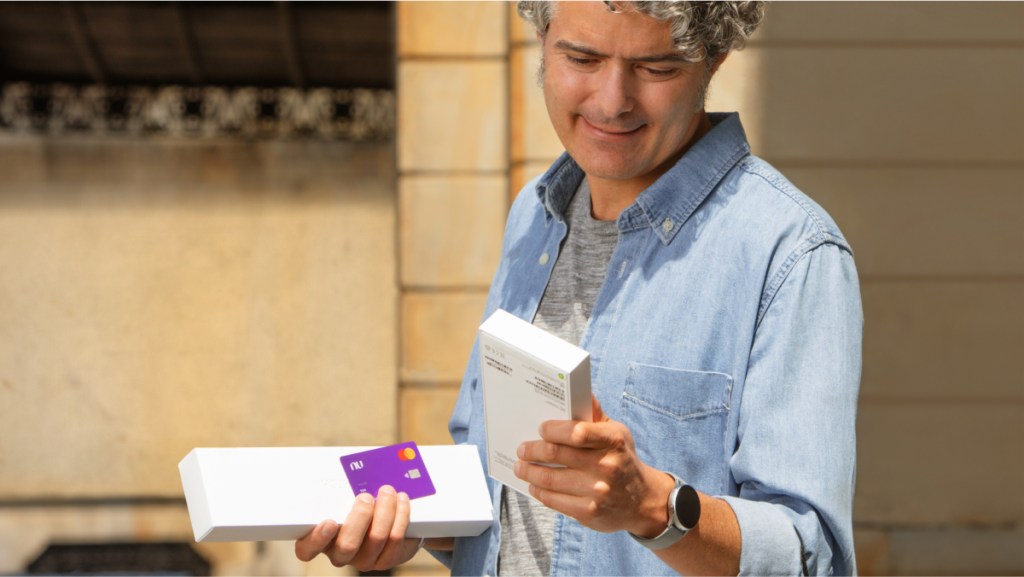 Beneficios Mastercard Gold: cuáles son y cómo usarlos Foto de hombre con la tarjeta de crédito Nu. Beneficios Mastercard Gold: cuáles son y cómo usarlos.