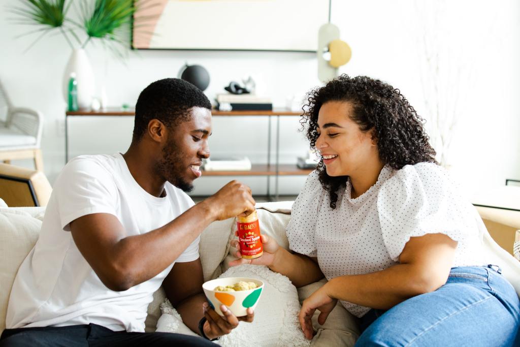 Vivir juntos: una pareja come en un sillón de un bowl y un frasco. Foto: No Revisions/Unsplash.