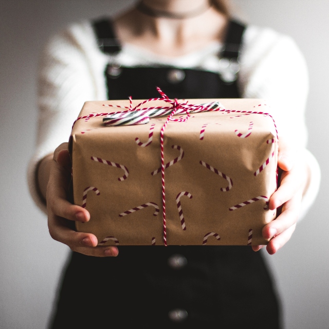 Una mujer vestida con un solero oscuro sostienen un paquete envuelto en papel cartón con motivos navideños. Compras navideñas: 10 consejos para ahorrar y empezar el año sin deudas