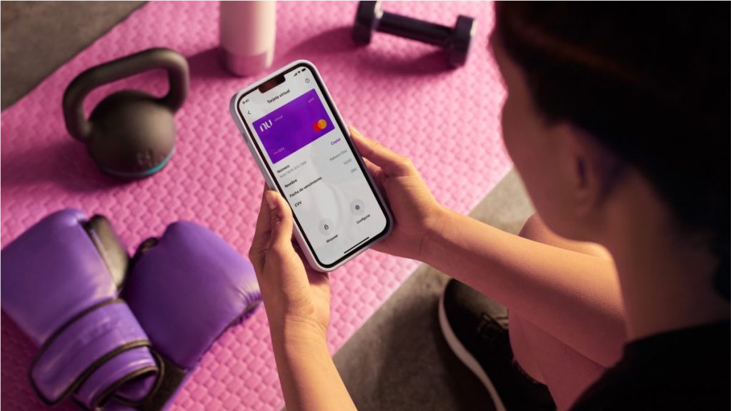 Vive más con Nu: la Tarjeta virtual Foto de mujer en su celular viendo la tarjeta virtual de Nu. ¿Por qué dan una tarjeta virtual?