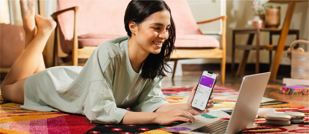 Vive más con Nu: cómo pagar la tarjeta Nu Foto de mujer sonriente y acostada con la app de Nu. Vive más con Nu: cómo pagar la Moradita Nu.